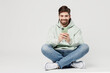 © ViDi Studio - Full body smiling happy cheerful young caucasian man wear mint hoody look camera hold in hand use mobile cell phone isolated on plain solid white background studio portrait. People lifestyle concept.