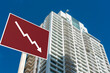 A sign showing an downward arrow in front of a highrise condominium or apartment. Concept of decreasing or slumping condo prices and value or a real estate bust.