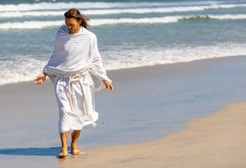 Wall Mural - Man with white robe and beard walks on the beach