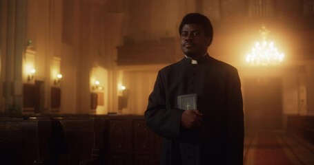 Wall Mural - Portrait of a Young Black Priest Holding the Holy Bible in His Hand and Looking at the Camera. A Servant of God Helping Lost Souls Find the Path of Righteousness through Faith, Devoted to Christianity