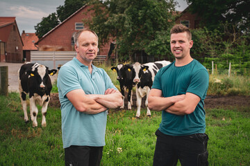 Poster - Landwirt mit seinem Sohn auf einer Wiese, im Hintergrund Rinder und ein Hof.