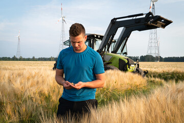 Poster - Junger Landwirt prüft in einen reifem Getreidefeld, die Körner, im Hintergrund steht ein Trecker.