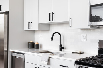 Wall Mural - A beautiful white kitchen detail shot with a tiled backsplash, white cabinets, stainless steel appliances, and black hardware and faucet.