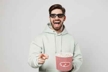 Poster - Young laughing fun cool caucasian woman wearing 3d glasses watch movie film hold bucket of popcorn in cinema point index fnger camera on you isolated on plain solid white background studio portrait.