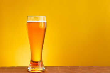 A glass of fresh beer on a yellow background, a favorite drink