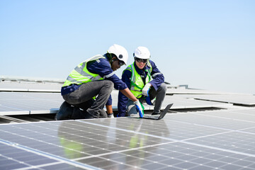 Engineer and technician using laptop checking and operating solar panels system on rooftop of solar cell farm power plant, Renewable energy source for electricity and power,