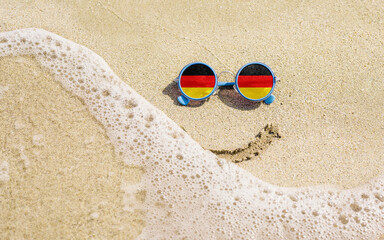 Wall Mural - Sunglasses with flag of Germany on a sandy beach. Nearby is a sea lightning and a painted smile. Travel and vacation concept for Germans