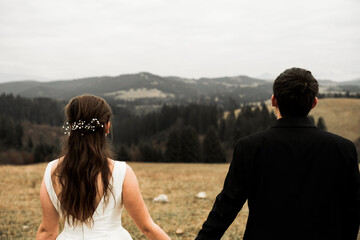 The bride and groom hold hands and look to the future in the middle of nature, the newlyweds walk together,wedding photography,until death do us part