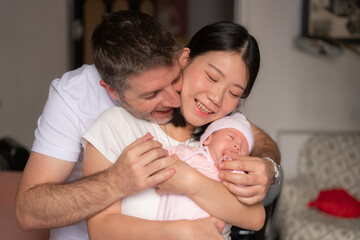 lifestyle portrait of young happy and attractive mixed ethnicity couple holding newborn baby girl smiling cheerful in parenting and love concept