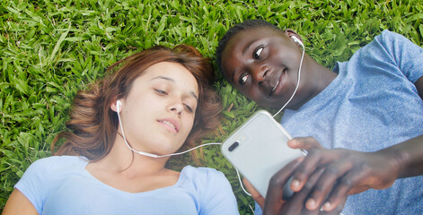 Wall Mural - African boy with caucasian girlfriend lying on the grass hearing music