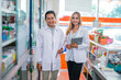 © Odua Images - two pharmacists in uniform holding tablets and clipboard standing next to a display case