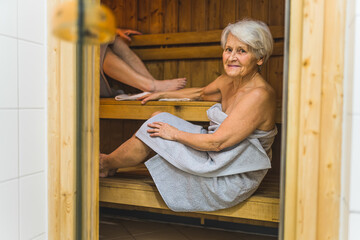 Senior woman wrapped in towels relaxing in the wooden spa sauna. High quality photo