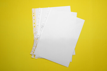 Punched pockets with paper sheets on yellow background, flat lay