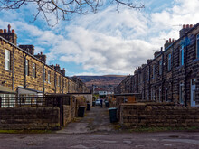 The Back Alley Of The Terraced Houses In A Street In Ilkley Town, With Ilkley Moor In The Background Under A Blue Sky With Scattered Clouds