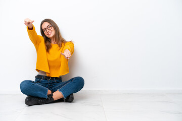 Wall Mural - Young caucasian woman sitting on the floor isolated on white background points finger at you while smiling