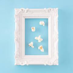 Wall Mural - Creative aesthetic arrangement made of popcorn in a retro white frame on a blue background. Minimal gallery or movie and entertainment concept.