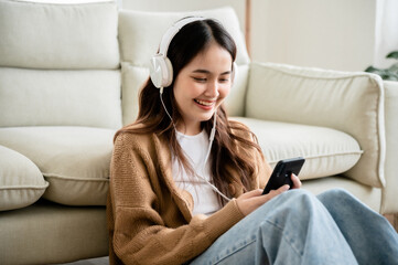 Wall Mural - Happy young asian woman relaxing at home. Female smile sitting on sofa and holding mobile smartphone. Girl using video call to friend