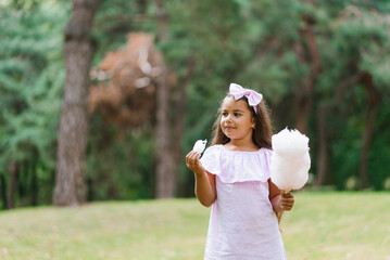 Wall Mural - Funny girl in pink dress eats cotton candy in summer in the park