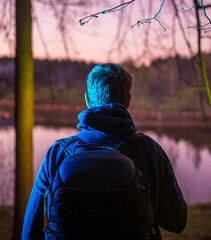 Backpack and man in blue light with pink background in forest