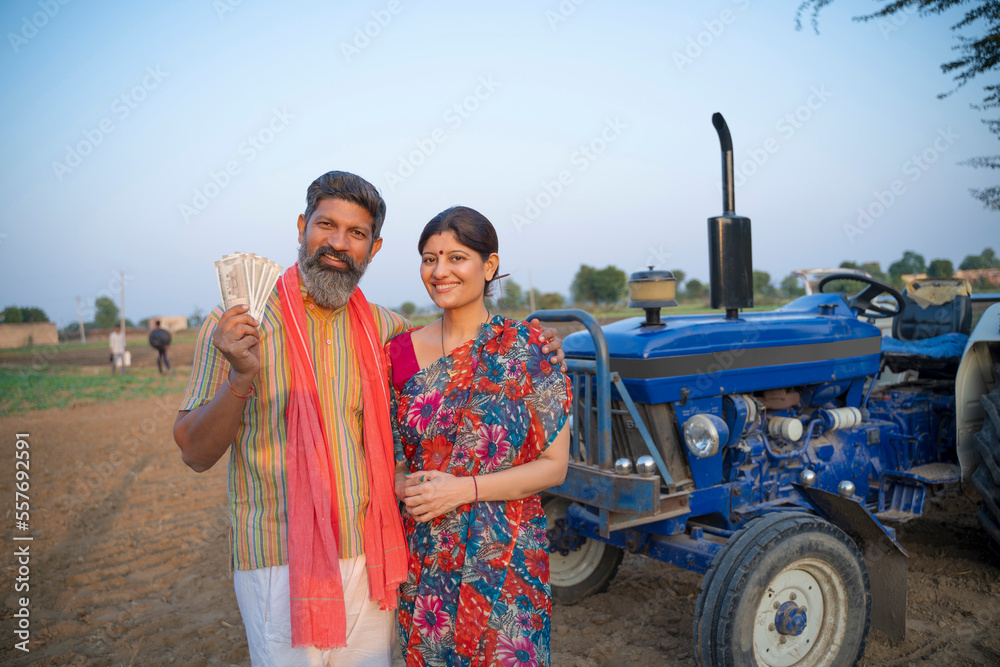 Indian farmer standing with wife near tractor and showing money at ...