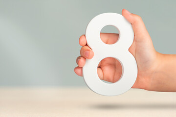 Fototapete - Eight in hand. A hand holds a white number 8 on a blurred background. Concept with number eight. Birthday 8 years, percentage, eighth grade or day, international women's day.
