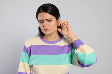 Poster - Young woman suffering from ear pain on light grey background