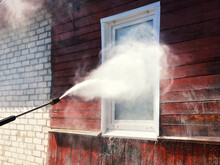 High Pressure Spray Gun Washing The White Window And Red Wall Of A Wooden Village House