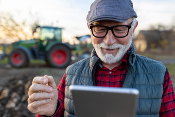 Canvas Print - Senior farmer with tablet in field with tractor in background