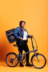 Wall Mural - Deliverywoman holding thermal backpack ready to deliver take away lunch to customer using bicycle. Pizzeria worker carrying bag while delivering fast food meal, takeout service and transportation