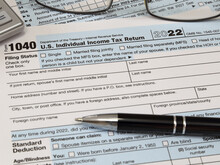 An IRS 1040 Tax Year 2022 Form Is Shown In 2023, Along With An Ink Pen, Calculator, And Glasses. The Internal Revenue Service Tax Filing Deadline In 2023 Is Scheduled For April 18.