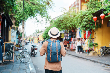 happy solo traveler sightseeing at hoi an ancient town in central vietnam, man traveling with backpa