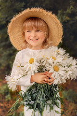 Wall Mural - a happy handsome blond boy in a straw hat with white daisies in his hands and a linen suit