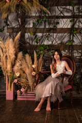 Teenager stylish girl in light pink dress barefoot sitting on armchair in mystery decorated room. Fashionable sad teen princess looking away indoors. Fantasy art photo, fairy tale concept. Copy space