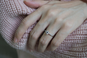 Wall Mural - Close up of an elegant engagement diamond ring on woman finger with pink sweater winter clothe. love and wedding concept. Soft and selective focus.