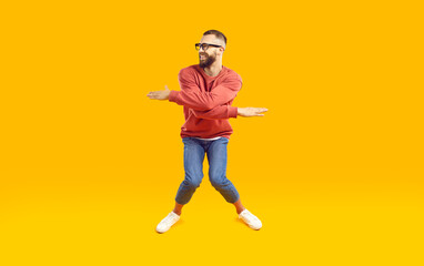 Wall Mural - cheerful, funny and energetic man showing humorous joking dance moves on orange background. full len