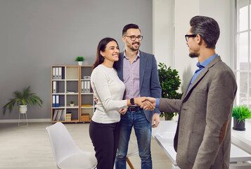 Happy young couple meeting with bank manager, lawyer, real estate agent, insurer. Smiling family couple greeting broker with handshake. Man and woman clients handshaking close deal or make agreement