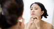 © Jirawatfoto - Problem skin. Concerned young asian women popping pimple on cheek while standing near mirror in bathroom. young asian women with acne