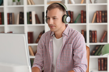 Wall Mural - Young man with headphones and computer studying online at home