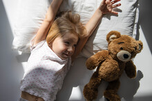 Little Girl Lies With A Soft Toy Teddy Bear. Top View, Flat Lay