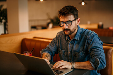 Wall Mural - Portrait of a journalist stylish guy writing a story in a workplace in loft styled coworking, casually dressed in a denim shirt, sitting alone.