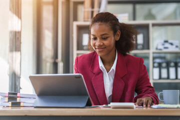 Wall Mural - Young african american businesswoman red suit working at desk and using digital tablet in the modern office. Start up SME worker concept.