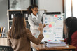 © Phushutter - Young diverse african american female coworkers working together on start up project. Business people meeting around a boardroom table discussing creative concept