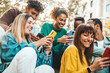 © Davide Angelini - Group of multiracial young people using smart mobile phone device outdoors - Happy university students watching cellphones sitting in college campus - Teenagers addicted to social media technology
