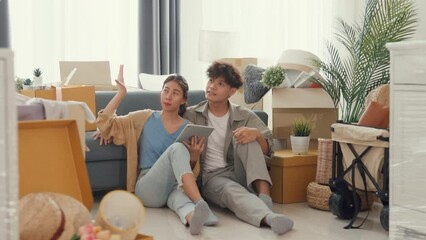 Wall Mural - Young happy Asia couple sit on sofa couch use digital tablet online shopping furniture from decoration store in living room at home. Husband wife move new house, Apartment Rent And Ownership Concept.