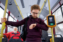 Portrait Of Ginger Curly Haired Wearing Glasses And Wrist Watch In Aubergine Sweater Male Rushing Trying To Fasten With Urban Transport. Hasty Rythm Of Life People Make Too Many Plans Getting Nervous