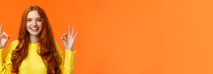 Wall Mural - Fashion, shopping, winter holidays concept. Attractive cheerful redhead woman showing okay gestures and smiling, everything alright, approve or like product, recommend online store, orange background