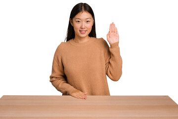 Wall Mural - Young asian woman sitting on a table isolated smiling cheerful showing number five with fingers.