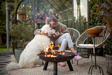 Young woman spends evening time with her cute white dog, sitting by the fire in garden at cozy and beautiful atmosphere