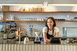 © Mix and Match Studio - Smiling friendly asian girl barista, wearing apron, working at counter, brewing filter coffee, managing cafe shop