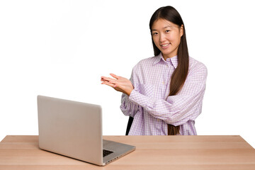 Wall Mural - Young student asian woman in a workplace with a laptop isolated holding a copy space on a palm.